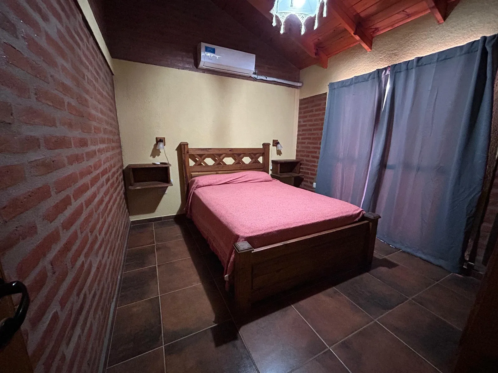 Dormitorio con cama matrimonial, techo de madera y paredes de ladrillo
